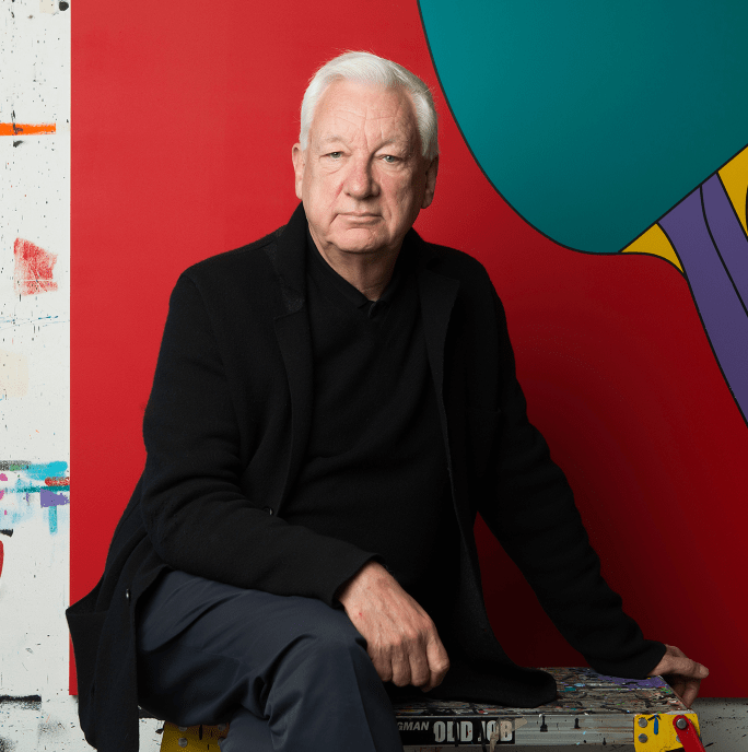 man with silver heair dressed in all black sits in front of one of his own paintings